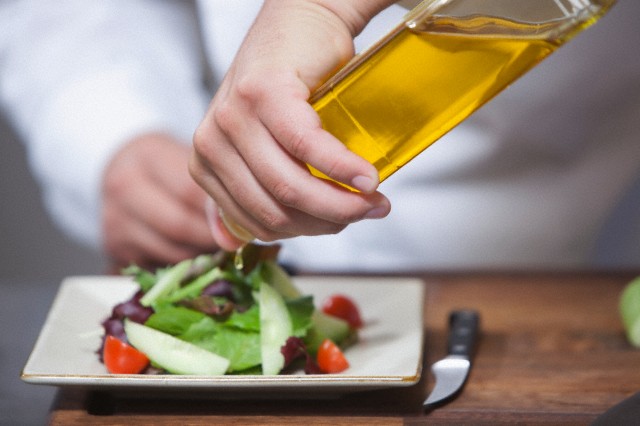 Mid- adult chef pours olive oil over side salad --- Image by © moodboard/Corbis
